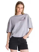 Remera oversize color gris con cuello redondo y mangas cortas. Presenta un estampado gráfico en el pecho con el logo de la marca Caterpillar y una pequeña etiqueta con el logo en el dobladillo.