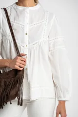 Blusa blanca de algodón con cuello mao, mangas largas abullonadas y detalles de encaje en el canesú, mangas y ruedo. Cierre frontal con botones.