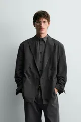 Blazer cruzado de corte relajado, confeccionado en mezcla de algodón y lino, en color gris oscuro. Presenta solapas de pico, bolsillos de parche en la cadera y cierre frontal de doble botonadura.