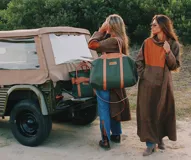 Bolso sport de lona color naranja con detalles y correas en cuero tostado. Cuenta con asas cortas y una correa larga ajustable y desmontable.