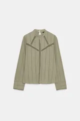 Camisa verde claro con cuello alto de puntilla, manga larga y detalles de entredoses calados en el pecho y los hombros. Cierre en la espalda con abertura y botón oculto.