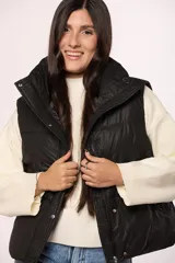 Chaleco puffer de nylon en color verde oliva, con cuello alto, cierre frontal con cremallera y botones a presión, y bolsillos laterales.