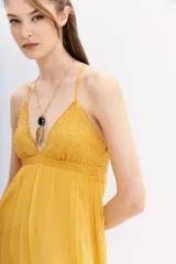 Vestido largo color mostaza con escote en V y breteles finos cruzados en la espalda. El corpiño está adornado con canutillos bordados, y la falda es fluida.