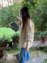 Sweater amplio de lana merino tejido a mano, color beige, con cuello redondo y mangas largas con diseño de trenzas.