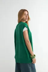 Chaleco de punto color verde, con escote en V y cierre frontal de botones negros. Presenta un diseño holgado con terminaciones acanaladas en el cuello, sisas y ruedo.