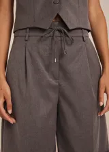 Bermuda gris de tejido plano con diseño entallado, cinturilla con trabillas y cordón, pinzas delanteras, bolsillos delanteros y traseros, cierre frontal y dobladillo en el ruedo.