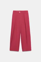 Pantalón de tiro bajo color fucsia, con pliegues delanteros, bolsillos frontales, pernera holgada y cierre frontal con cremallera y botón.