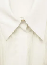 Camisa color crema de corte recto, con cuello camisero, cierre frontal oculto con botones, panel frontal con textura plisada, mangas largas con puños abotonados y tejido fluido.