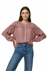 Camisa de color rosado con diseño plisado en la parte superior y volados en los hombros. Presenta cuello a la base, cierre frontal con botones y mangas largas abullonadas con puños elásticos.