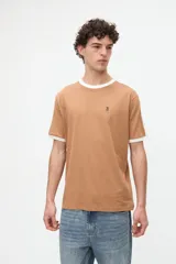 Remera de manga corta azul con cuello redondo, puños y bandas en los hombros en color tostado. Presenta un pequeño bordado rojo en el pecho y está confeccionada en suave jersey de algodón con calce clásico.