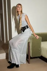 Vestido largo plateado de gasa con lurex, corte holgado, mangas cortas y cuello redondo. Incluye cinturón ancho de cuero negro con hebilla dorada.