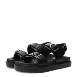Sandalias de plataforma plana Miss Carol modelo Naira, color negro con doble tira ajustable con hebillas metálicas plateadas y suela dentada.