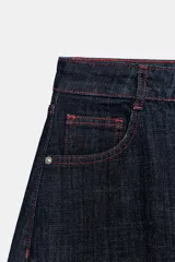 Jeans de tiro alto color azul oscuro, con cinco bolsillos y pernera holgada que se estrecha hacia el tobillo. Presenta pespuntes en color rojo y cierre frontal con cremallera y botón.