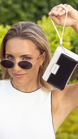 Billetera mediana bicolor en blanco y negro, confeccionada en símil cuero. Cuenta con tapa frontal con detalle de placa metálica con logo grabado, cierre perimetral y correa de muñeca extraíble.