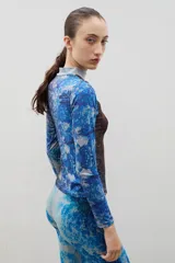 Polera de cuello alto y manga larga, confeccionada en tela sublimada con un estampado artístico que evoca un paisaje boscoso en tonos azules y marrones.