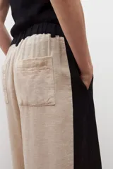 Pantalón ancho de lino color beige con paneles laterales negros y tajos en el ruedo.