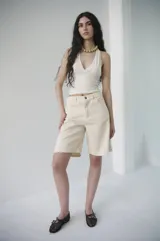 Bermuda de denim azul claro, de tiro medio y largo a la rodilla, con calce relajado y silueta amplia. Cuenta con bolsillos delanteros y traseros, y cierre frontal con botón y cremallera.