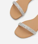 Sandalia plana color nude con tira fina con aplicación de strass y mini espejos, cierre en el tobillo, puntera redonda y taco bajo plano.