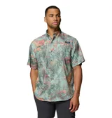 Camisa de manga corta Columbia modelo Super Tamiami, con estampado tropical de hojas en tonos verdes, rosados y naranjas. Presenta cuello abotonado, cierre frontal con botones y bolsillo en el pecho con logo de la marca.