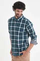 Camisa de manga larga con estampado de cuadros en tonos verde petróleo, blanco y líneas finas en color ocre. Presenta cuello clásico con botones y puños con detalle en contraste.