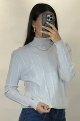 Buzo de hilo de punto con diseño de trenzas verticales, cuello alto y cadena metálica decorativa incorporada en la parte frontal.