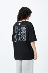 Remera blanca de corte amplio con mangas cortas y estampado con la frase "Unlearn" en el frente y gráfico en la espalda.