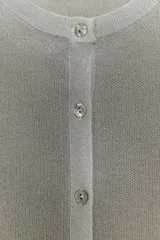 Chaqueta de punto de manga larga y cuello redondo, color gris claro con un sutil brillo metálico y efecto degradado en el tejido. Cierre frontal con botones plateados.