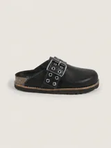 Zueco de cuero negro con diseño de punta redonda y tira ajustable en el empeine con hebilla metálica y ojales decorativos. Interior forrado en cuero y suela con vira reforzada.