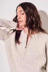 Sweater de punto color crema, con cuello redondo y cierre metálico a la mitad del frente.