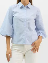 Camisa de algodón con patrón de rayas verticales, cuello camisero clásico y cierre frontal con botones. Presenta detalles metálicos aplicados en el frente y mangas, con mangas 3/4 abullonadas y ruedo recto.