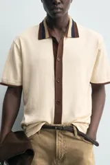 Camisa de punto de algodón con corte relajado, cuello solapa y manga corta. Presenta un diseño bicolor en tonos beige y marrón, con cierre frontal de botones.