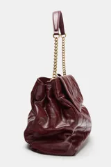 Bolso tipo shopper color borravino con diseño acolchado y pespuntes en rombos. Cuenta con solapa frontal y una correa de hombro que combina material sintético con una cadena metálica dorada.