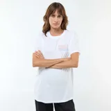 Camiseta de lactancia blanca de manga corta, con cuello redondo y estampa frontal con texto y diseño de tablero de ajedrez. Presenta aberturas laterales discretas para facilitar la lactancia.