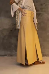 Falda larga de cuero genuino en color mostaza, con diseño de tiro bajo y silueta recta. Presenta bolsillos funcionales delanteros y traseros, cierre con botón y múltiples tajos que aportan movimiento y comodidad.