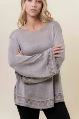 Sweater de tejido liviano con efecto lurex, color beige o gris claro metalizado. Presenta cuello redondo, mangas amplias estilo campana y terminaciones en punto elástico con diseño de cuadros en puños y ruedo.