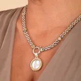 Conjunto compuesto por una cadena de eslabones gruesos en plata y oro, y un dije circular con centro de nácar y borde en oro y plata.