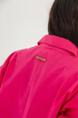 Camisa blanca de mangas largas con cuello clásico y cierre con botones. Presenta detalles de fruncido vertical en la parte delantera y cordones ajustables en los laterales. Corte holgado.