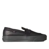 Championes Vans tipo mocasín de cuero negro, con diseño inspirado en el skate y estética clásica. Presenta detalles de tachuelas metálicas en la lengüeta, construcción vulcanizada y suela waffle de goma gris oscuro.