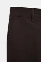 Pantalón de tiro bajo color marrón, con bolsillos frontales, falsos bolsillos traseros de vivo y cierre delantero con cremallera y gancho metálico.