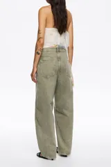 Pantalón de denim color verde oliva, tiro bajo, corte barrel (tobillero y ancho), con cierre de botones frontales y diseño de cinco bolsillos.