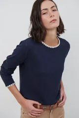 Remera de manga larga en color azul marino, confeccionada en tejido suave. Presenta un delicado detalle de bordado festoneado en color blanco tanto en el cuello redondo como en los puños, aportando un toque distintivo a esta prenda básica.