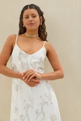 Vestido largo blanco de lino con tirantes finos, escote en V y delicado bordado plateado con motivos florales y brillantes en toda la prenda.
