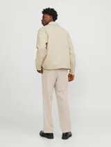 Chaqueta color crema con cuello camisero, cierre frontal con cremallera metálica, bolsillos de parche con solapa abotonada en el pecho y corte recto.