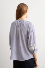 Blusa de manga larga con estampado de rayas verticales en tonos celestes y blancos. Presenta un escote en V con cierre frontal de botones y detalles de bordados florales en color crema en el frente y en los puños.
