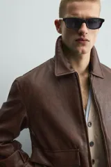 Sobrecamisa de corte relajado confeccionada en tejido efecto piel color marrón. Presenta cuello solapa, cierre frontal con cremallera, mangas largas con puños abotonados y dos bolsillos de plastrón con solapa en la parte frontal.