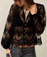 Camisa de encaje negro con diseño floral, cuello en V, cierre frontal con botones y mangas largas abullonadas con puños elásticos.