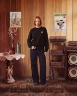 Buzo de cuello redondo color negro, con calce regular y puños y cintura acanalados. Presenta un pequeño logo estampado en el pecho con diseño de cuadros y letras amarillas.