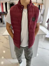 Chaleco puffer de nylon color bordó, con cuello alto, cierre frontal y bolsillos. Cuenta con un parche redondo con la inscripción "TURK" en el pecho.