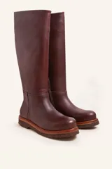 Bota de caña alta confeccionada en cuero vacuno suave, con diseño minimalista y suela de goma robusta. Presenta costuras visibles en la zona del empeine y un taco bajo cuadrado.