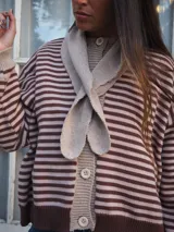 Sweater de punto a rayas horizontales blancas y azul marino, con cuello redondo, cierre frontal con botones y mangas largas con puños y detalles en tono azul.